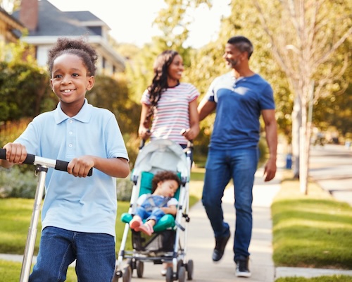 boy on scooter with family walking behind him